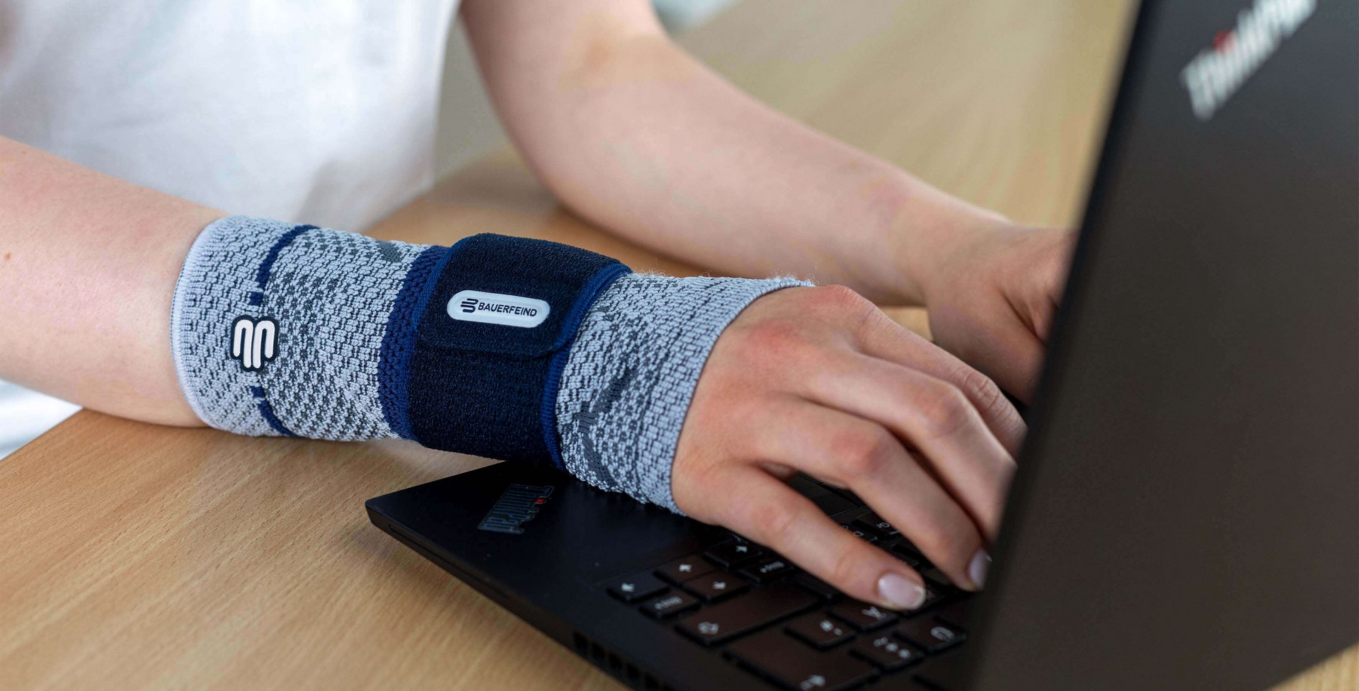 Bildausschnitt einer Frau am Laptop, die am rechten Handgelenk eine ManuTrain Bandage von Bauerfeind trägt. Diese bietet Unterstützung bei Mausarm-Beschwerden.